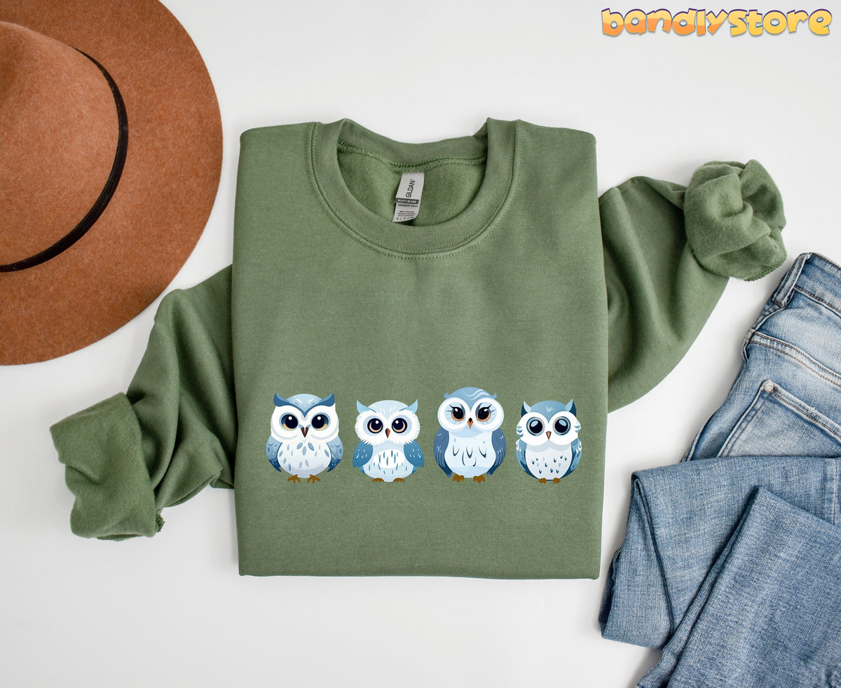 Cute Snow Owl Sweatshirt in military green flat-laid beside a brown hat and blue jeans.