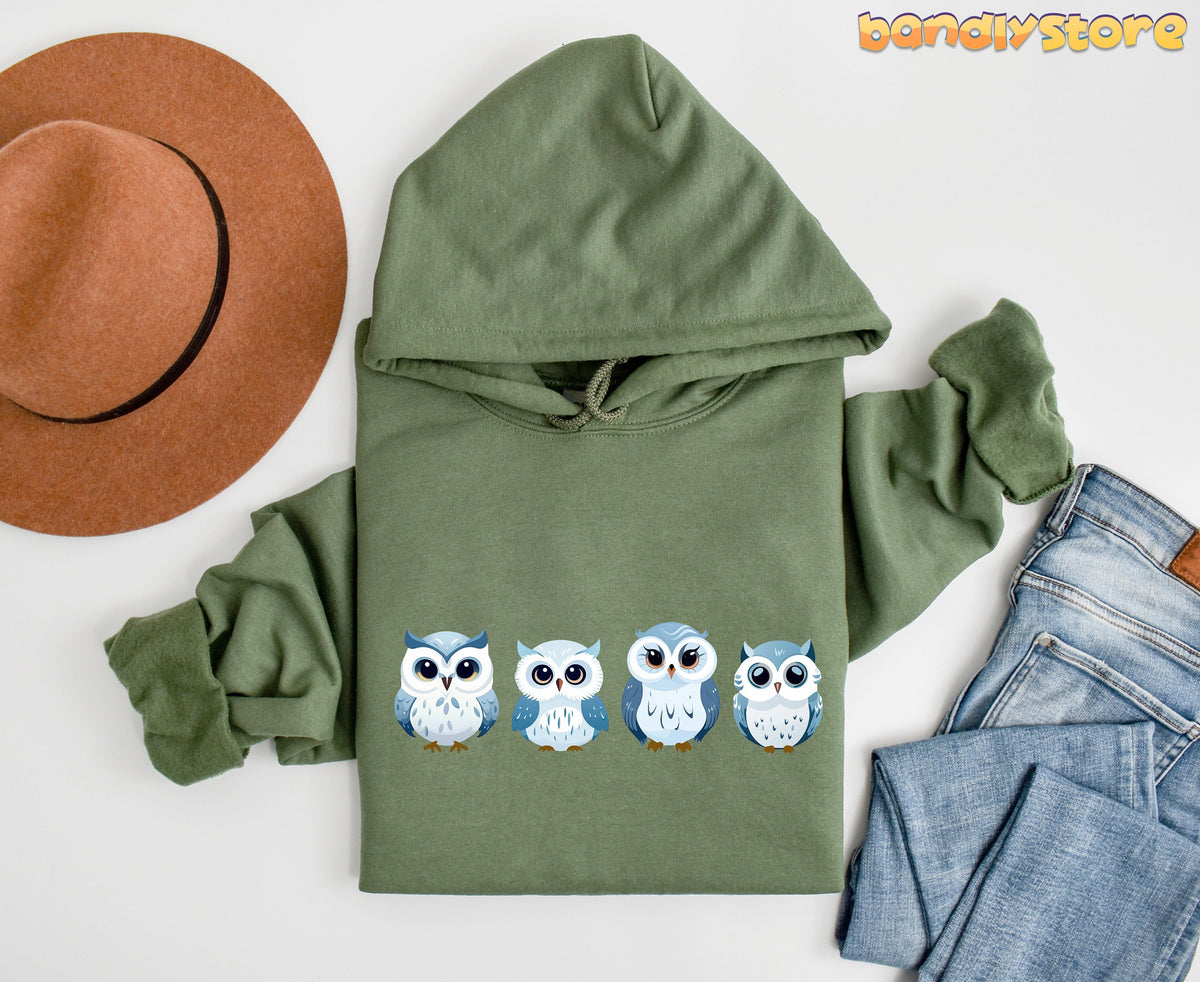 Cute Snow Owl Hoodie in military green laid flat beside a brown hat and blue jeans.