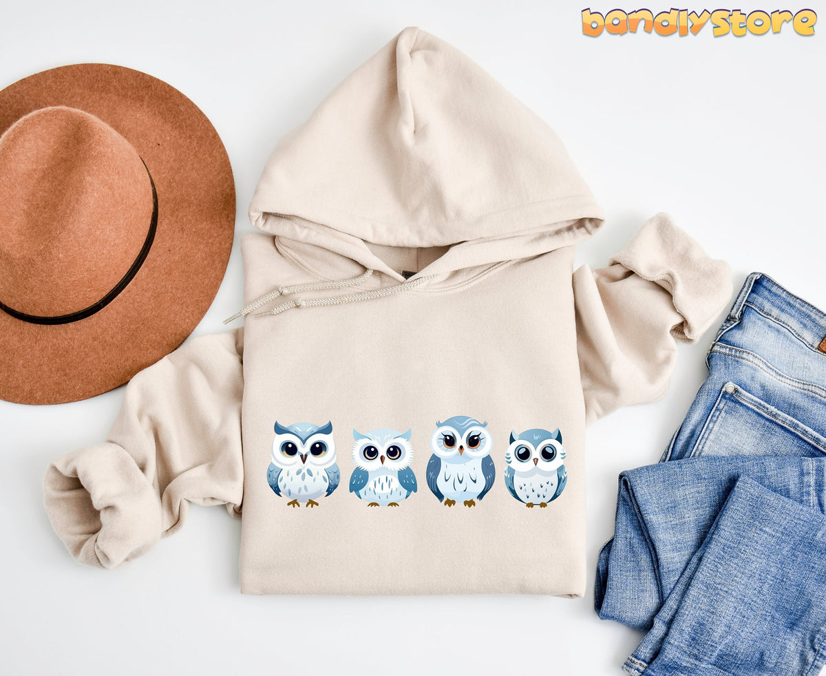 Cute Snow Owl Hoodie in sand, flat lay with brown hat left and blue jeans right.