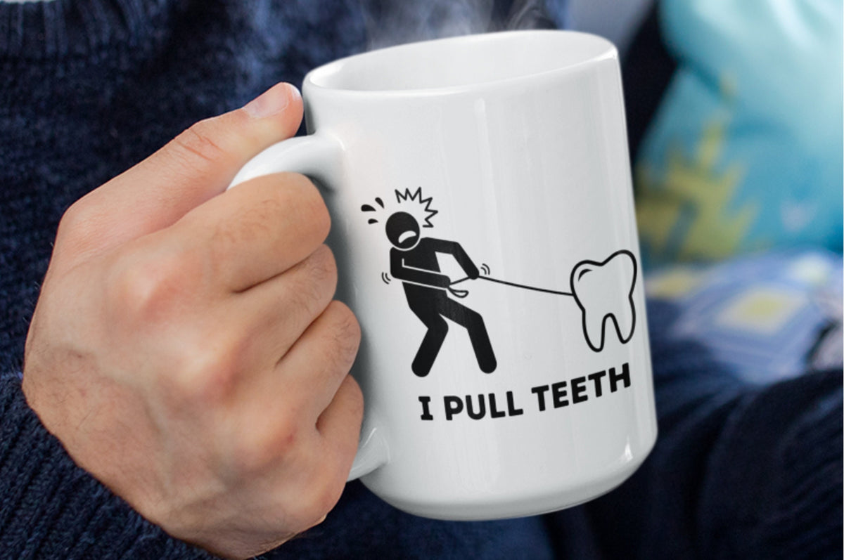 I Pull Teeth Dentist Mug held close by a hand in a knit sweater with steam rising beside a patterned cushion.