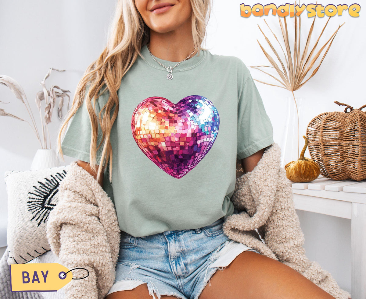 Disco Ball Heart T-Shirt in bay, front view on model seated among dried plants and wicker pumpkins.