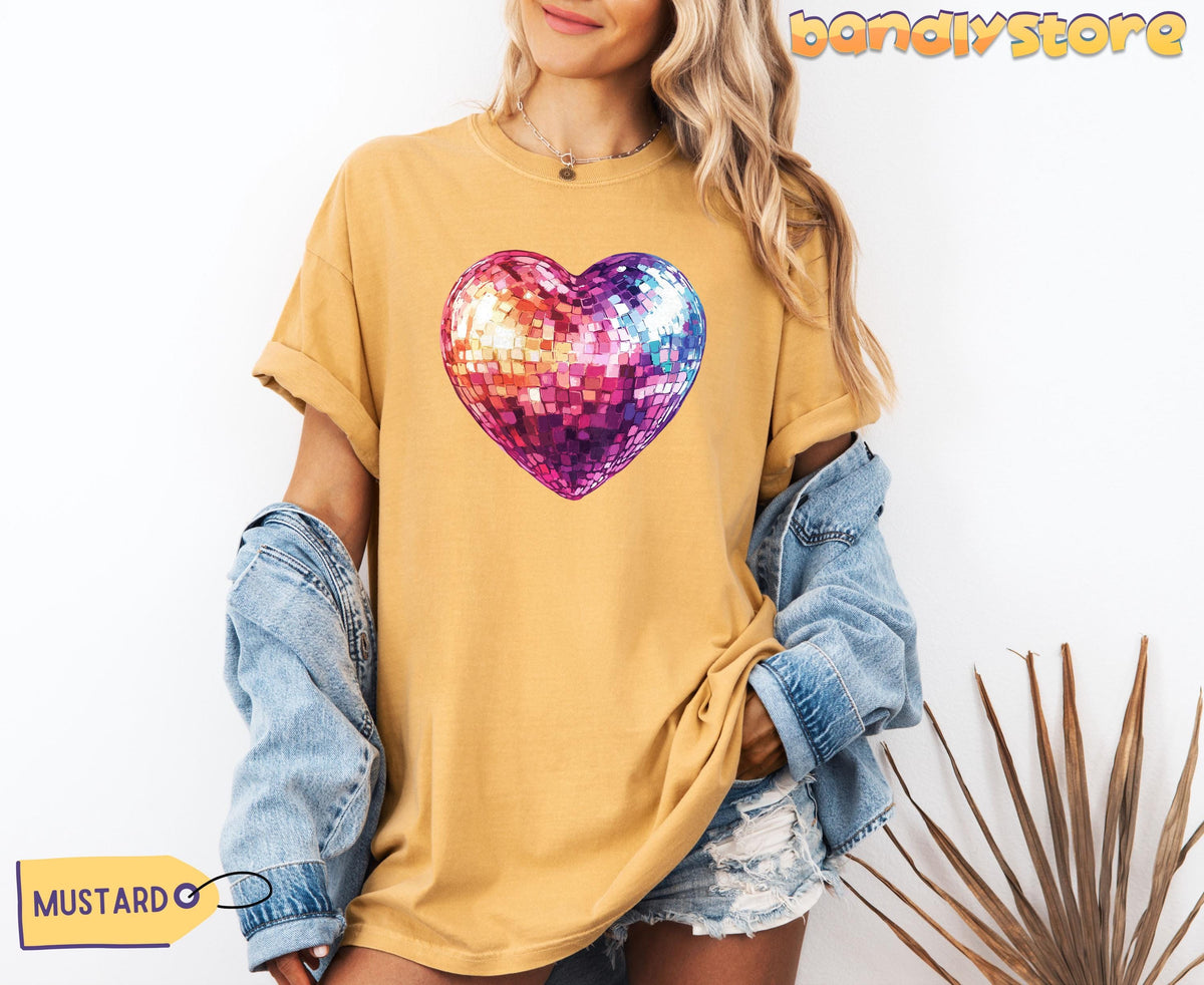 Disco Ball Heart T-Shirt in mustard on a forward-facing model with denim jacket and shorts next to a plant on white.