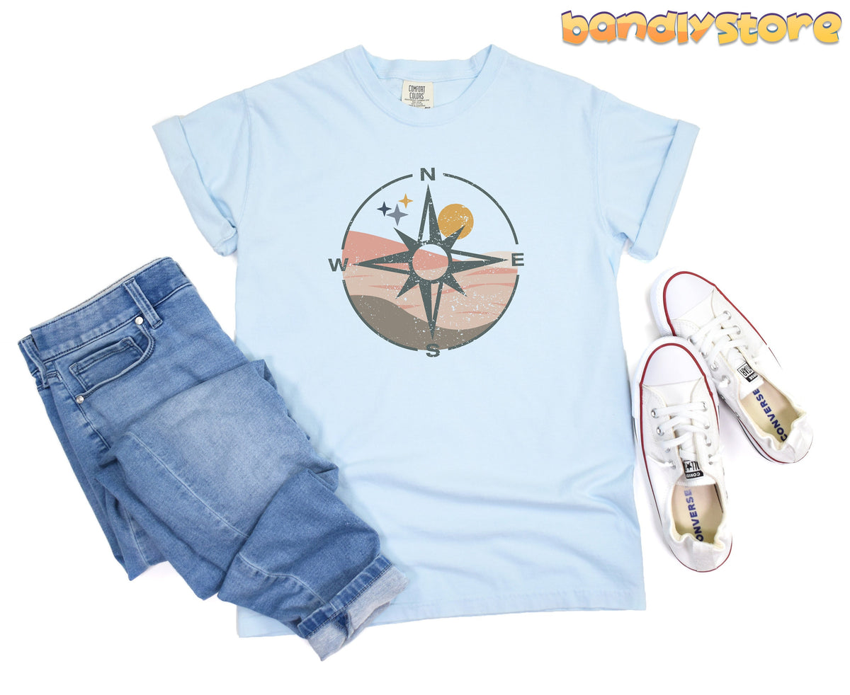 Distressed Compass T-Shirt in chambray laid flat beside folded jeans and white sneakers.