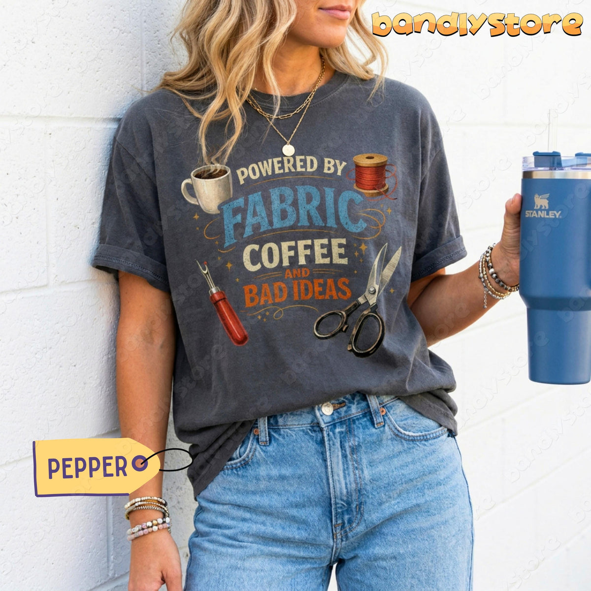 Powered By Fabric, Coffee And Bad Ideas T-Shirt in Pepper on woman against white brick wall holding blue tumbler.