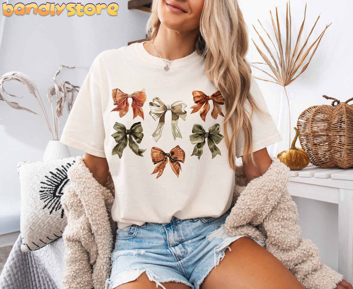 Fall Coquette Bow T-Shirt in ivory on seated model amid dried plants, wicker pumpkins and fall decor.