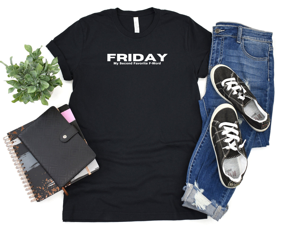 Friday My Second Favorite F-Word T-Shirt in black flat lay next to a plant, notebooks, jeans and sneakers.