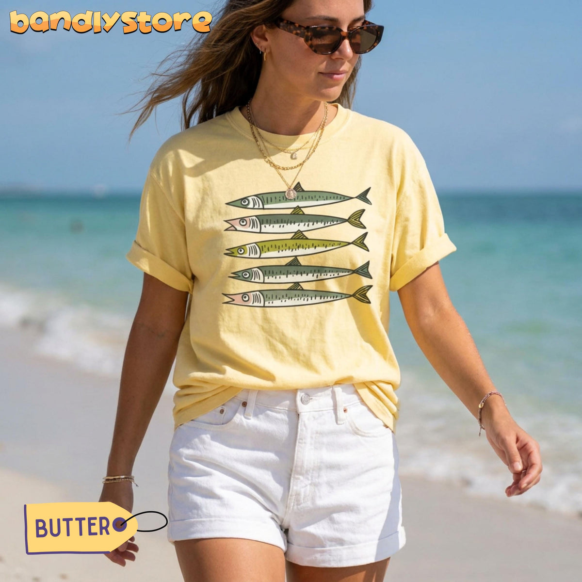 Funny Sardines T-Shirt in butter worn by a woman standing on a beach with ocean behind.