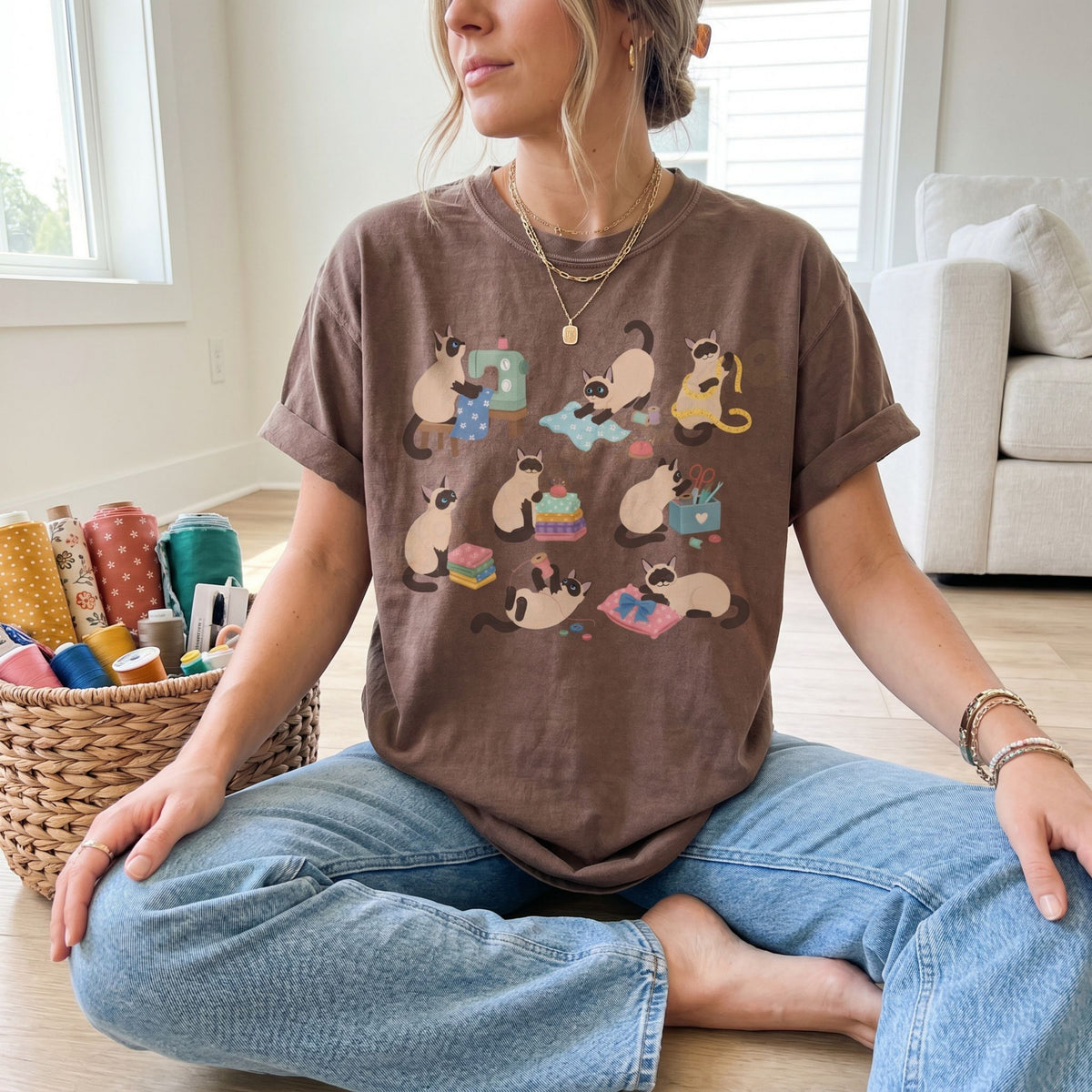 Funny Sewing Siamese Cats T-Shirt in espresso, front view on seated person beside sewing basket on wooden floor with sofa.