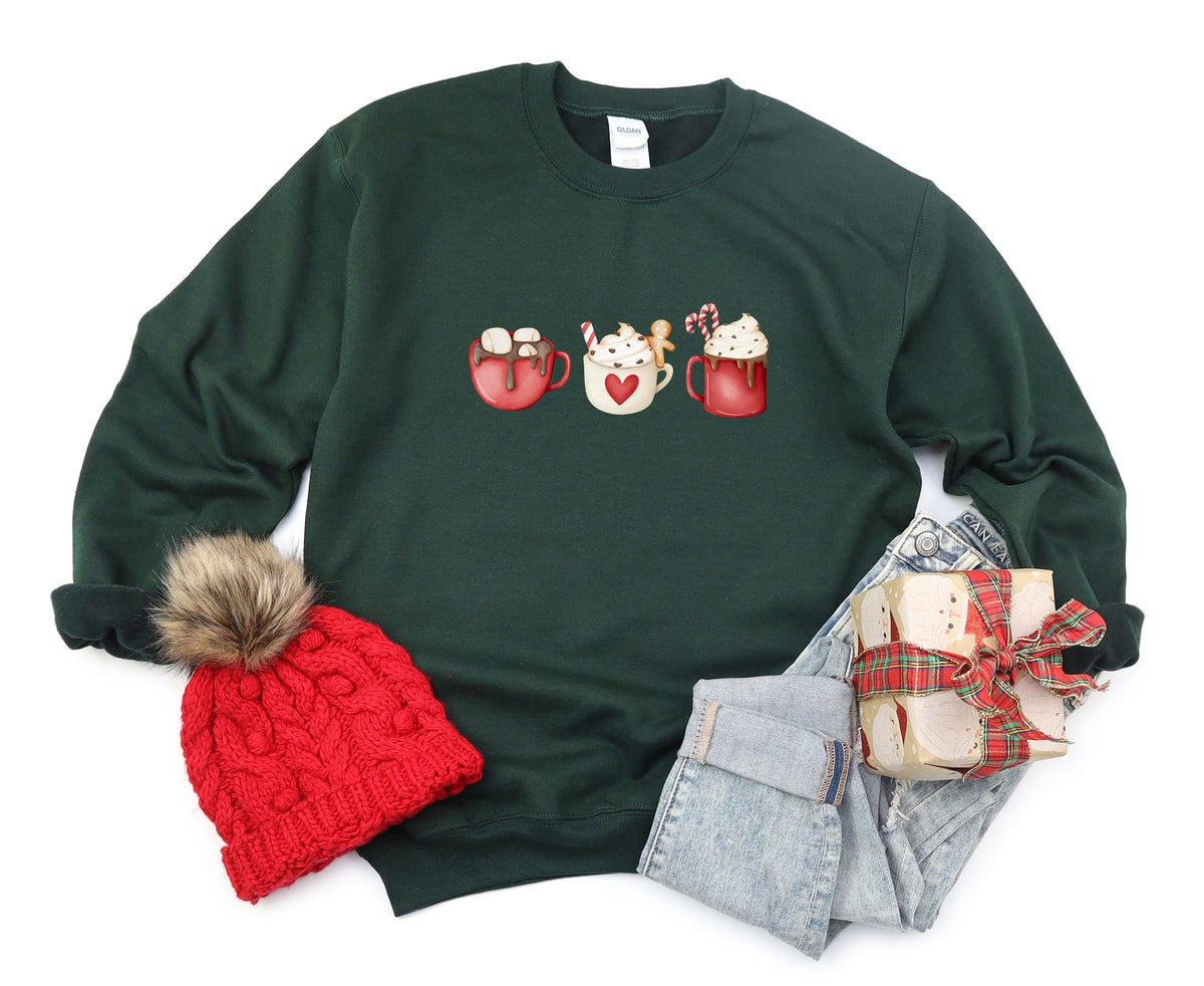 Coffee Cocoa and Gingerbread Cookies Sweatshirt in forest green, flat-laid with red pom beanie, folded jeans, and wrapped gift.