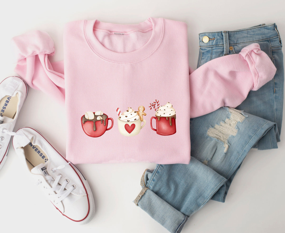 Coffee Cocoa and Gingerbread Cookies Sweatshirt in light pink, flat-laid with white sneakers and blue jeans.