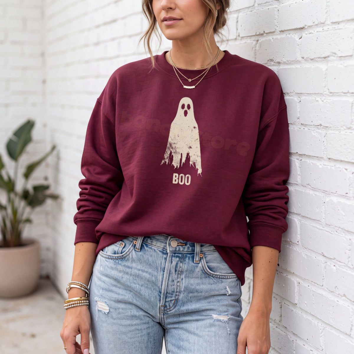 Grungy Ghost Sweatshirt in maroon, worn front-facing against a white brick wall with a potted plant nearby.
