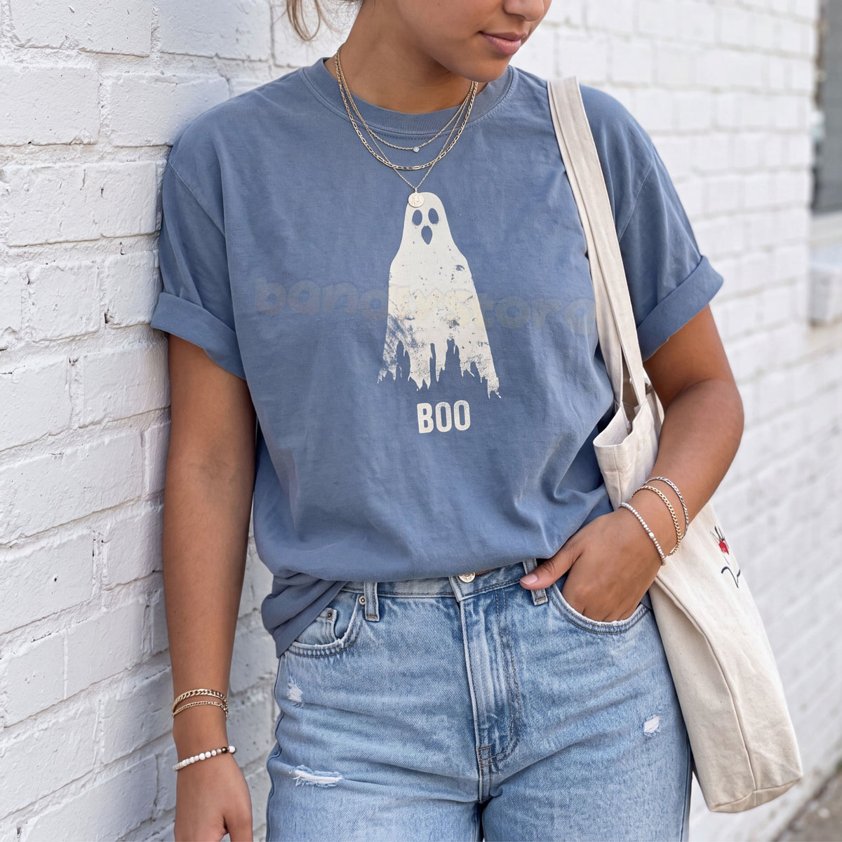Grungy Ghost T-Shirt in Blue Jean on a person leaning against a white brick wall with a tote bag.