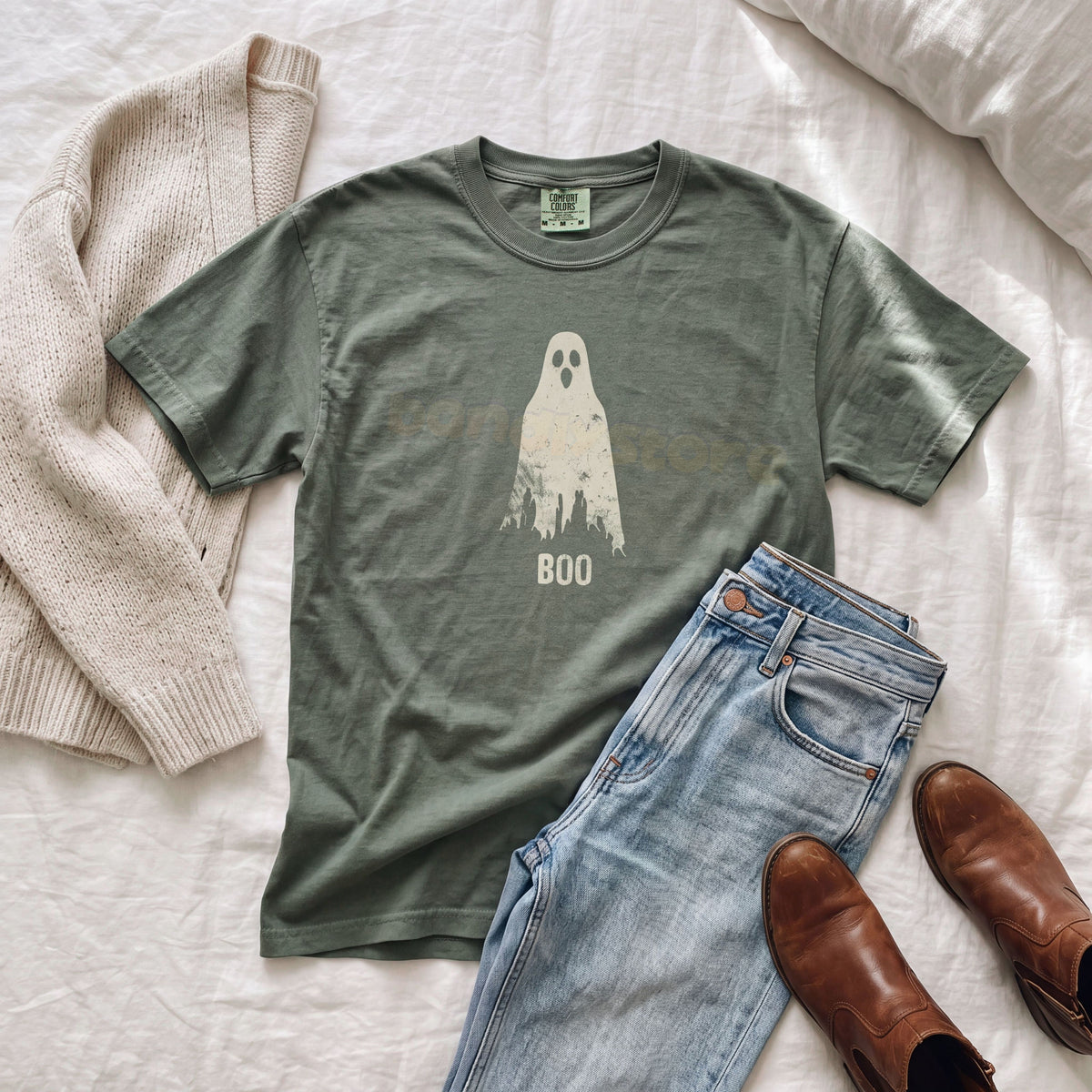 Grungy Ghost T-Shirt in moss flat on white bedding next to sweater, jeans and boots.