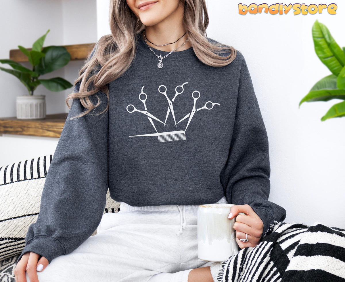Hairstylist Crown Sweatshirt in Dark Heather on a seated woman holding a mug amid indoor plants.