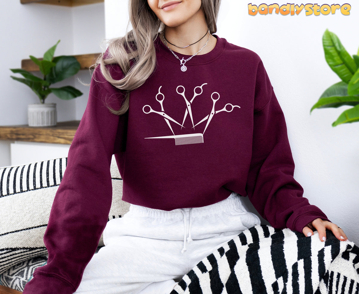 Hairstylist Crown Sweatshirt in maroon on a seated woman indoors amid plants and striped pillows.