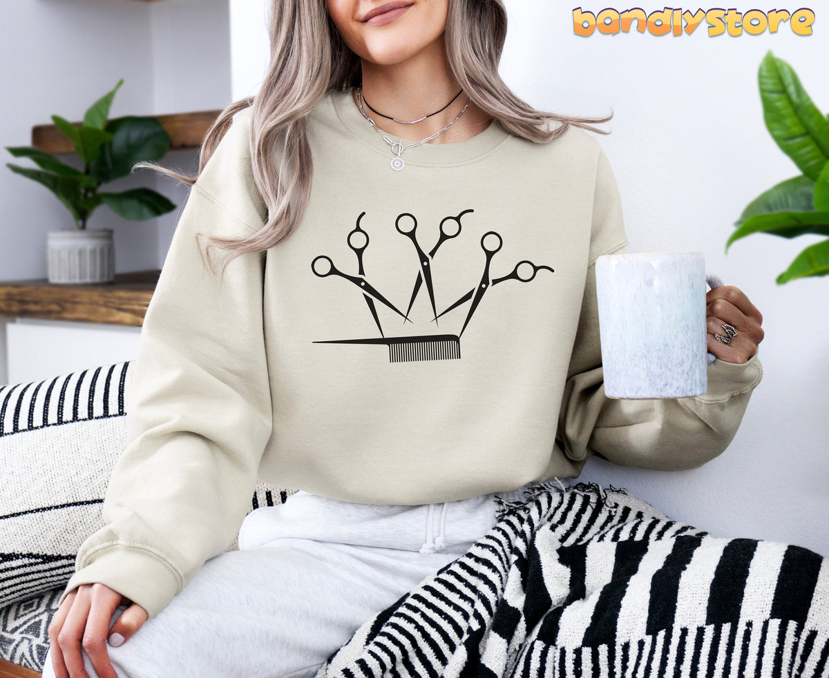 Hairstylist Crown Sweatshirt in sand on seated woman holding mug amid plants and striped textiles.