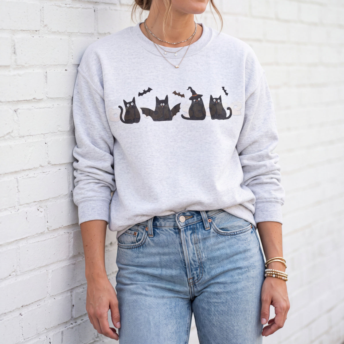 Halloween Black Cats And Bats Sweatshirt in ash on a person leaning against a white brick wall
