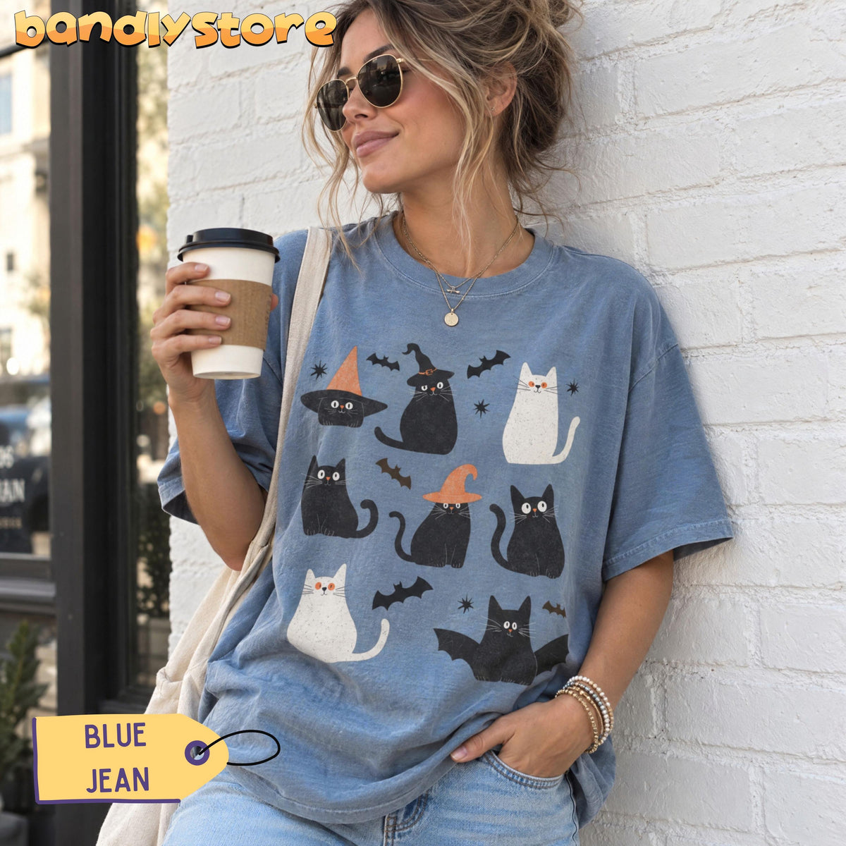 Cute Halloween Black Cats T-Shirt in Blue Jean worn by a woman leaning against a white brick wall holding a coffee cup.