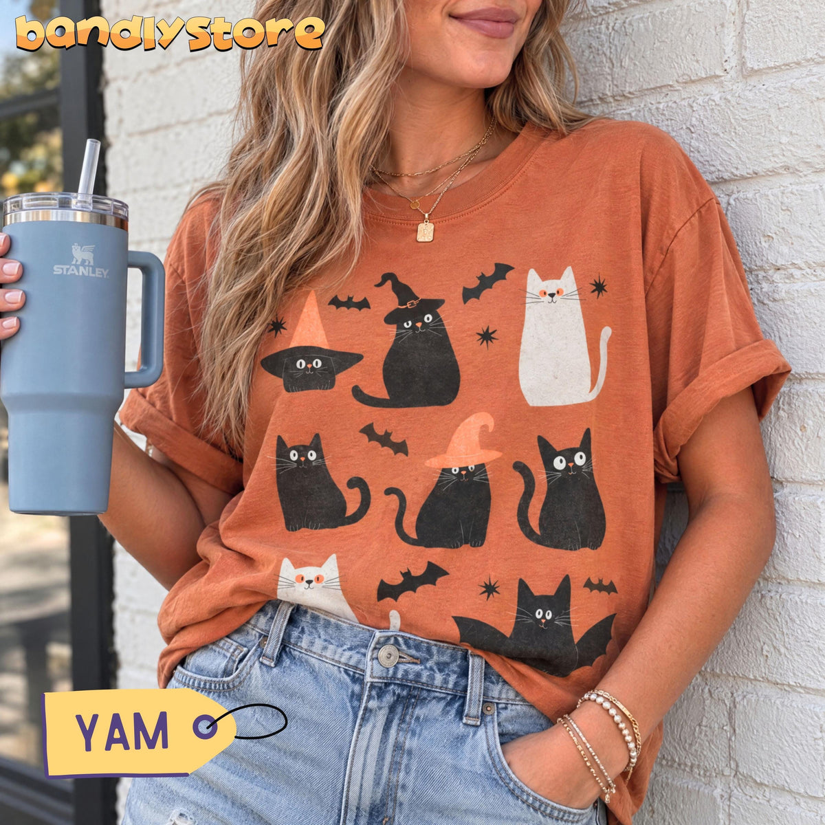 Cute Halloween Black Cats T-Shirt in yam worn by a woman holding a tumbler against a white brick wall.
