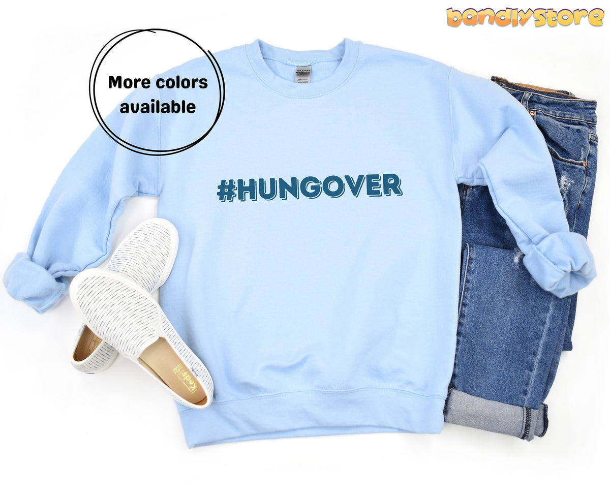 Hashtag Hangover Sweatshirt in light blue laid flat with white slip-ons and blue jeans beside it.