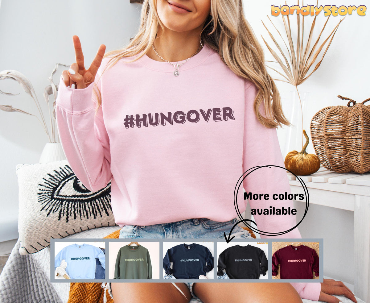 Hashtag Hangover Sweatshirt in light pink worn by a woman making a peace sign beside dried plants and a pumpkin.