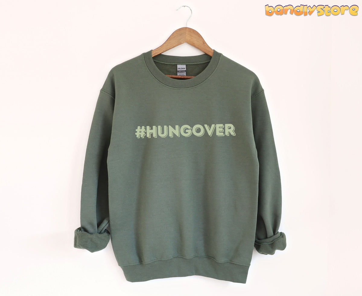 Hashtag Hangover Sweatshirt in military green hanging on a wooden hanger against a plain white wall.