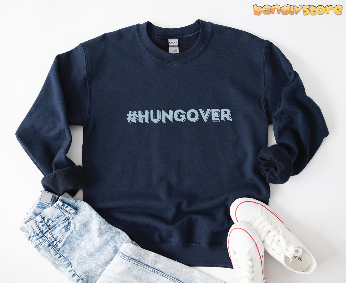 Hashtag Hangover Sweatshirt in navy laid flat on white background beside jeans and sneakers.