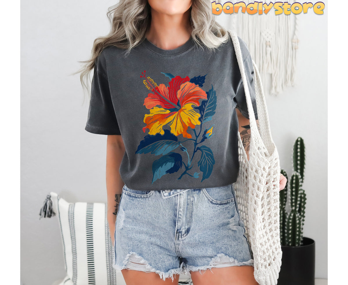 Hibiscus Flower T-Shirt in pepper on a model facing forward indoors by a cactus, pillow and white woven bag.