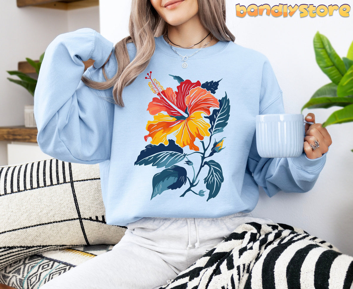 Hibiscus Flower Sweatshirt in light blue on a seated person holding a mug amid cushions and plants.
