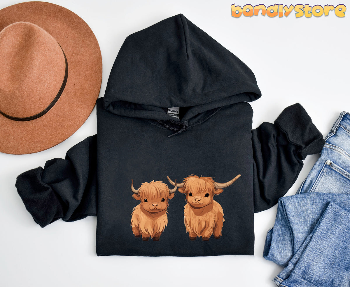 Highland Cow Hoodie black flat lay overhead beside brown hat and blue jeans on white.
