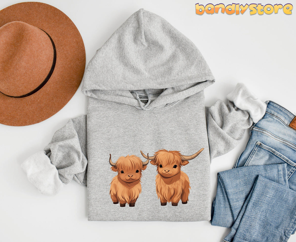 Highland Cow Hoodie in Sport Grey laid flat on a white background next to a brown hat and blue jeans.