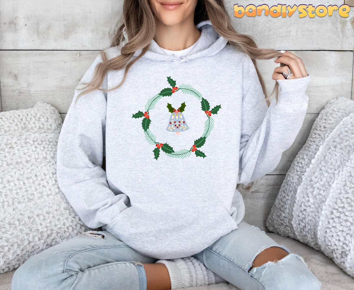 Holly Wreath Hoodie in ash on a person sitting cross-legged against wood panels with fluffy pillows.