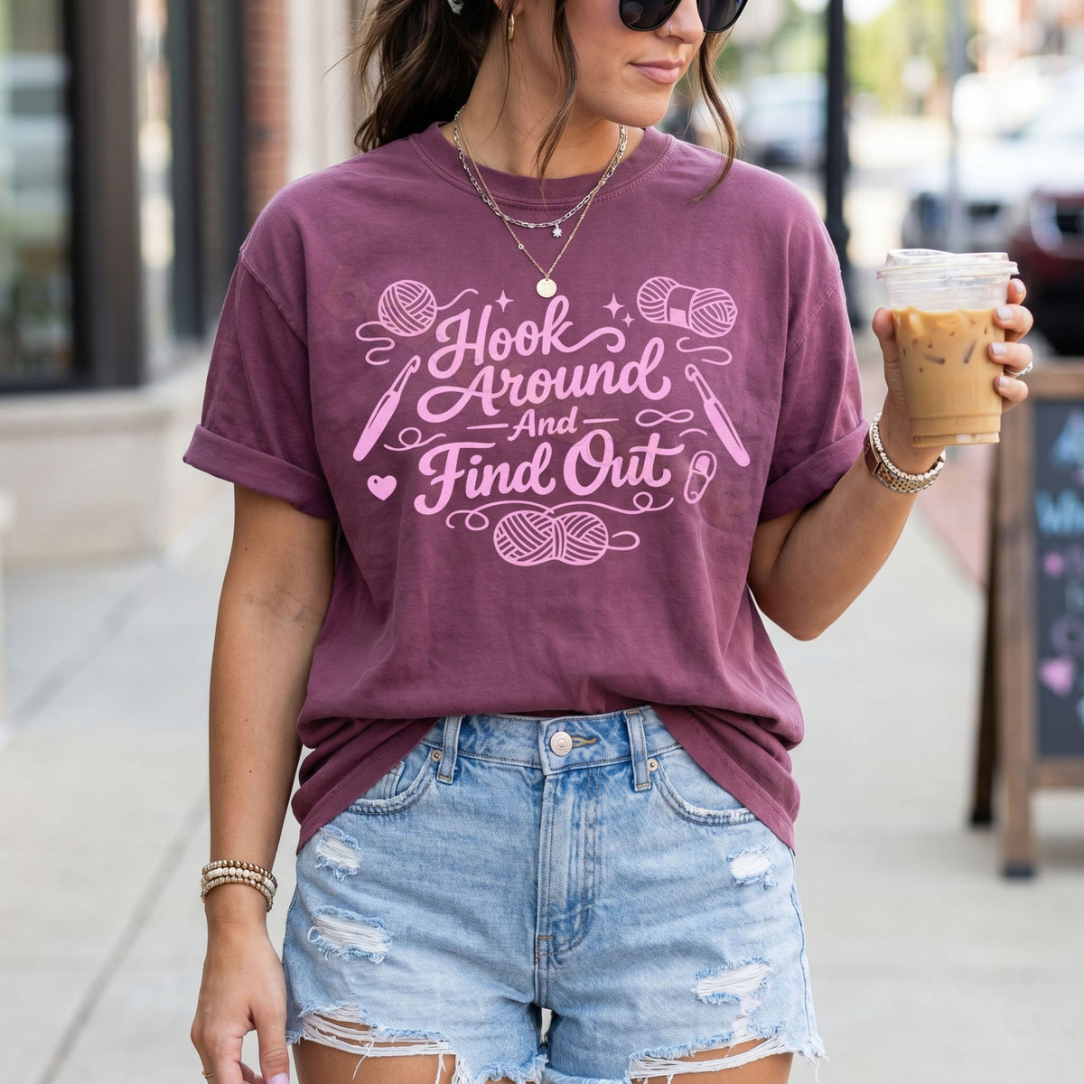 Hook Around And Find Out T-Shirt in Berry, worn outdoors by a woman holding iced coffee, torso view.