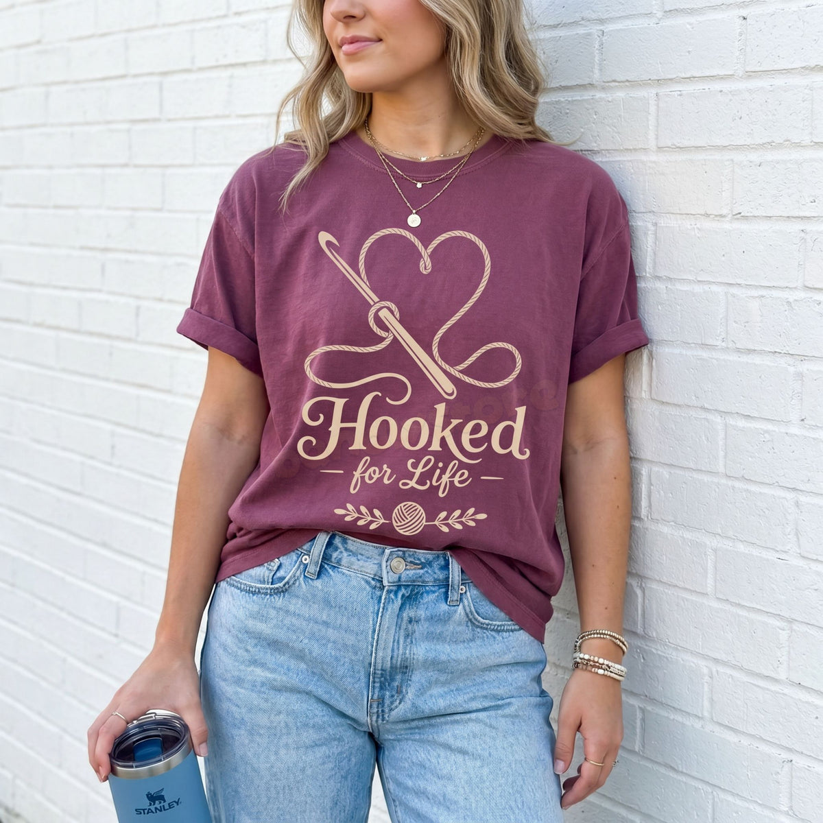 Hooked For Life T-Shirt in berry on a woman leaning against a white brick wall holding a tumbler.