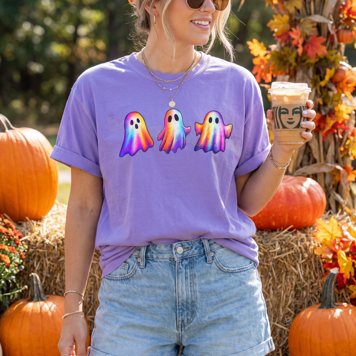 Iridescent Ghosts T-Shirt in violet worn by a person facing forward outdoors among pumpkins and hay bales holding a drink.