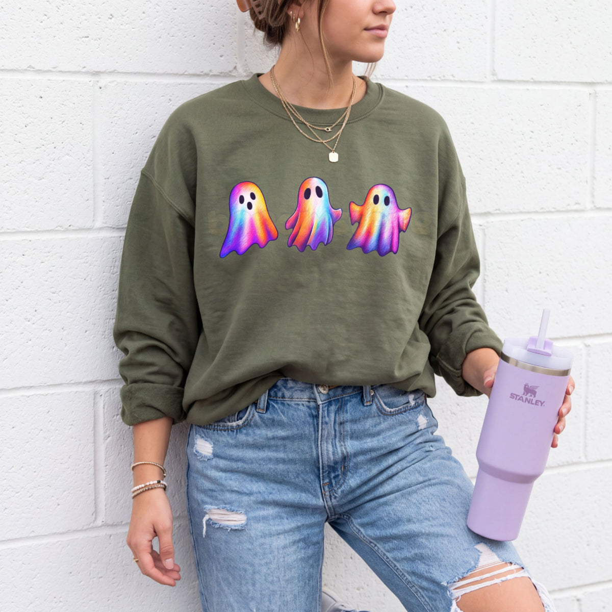 Iridescent Ghosts Sweatshirt in Military Green on a person leaning against a brick wall holding a tumbler.