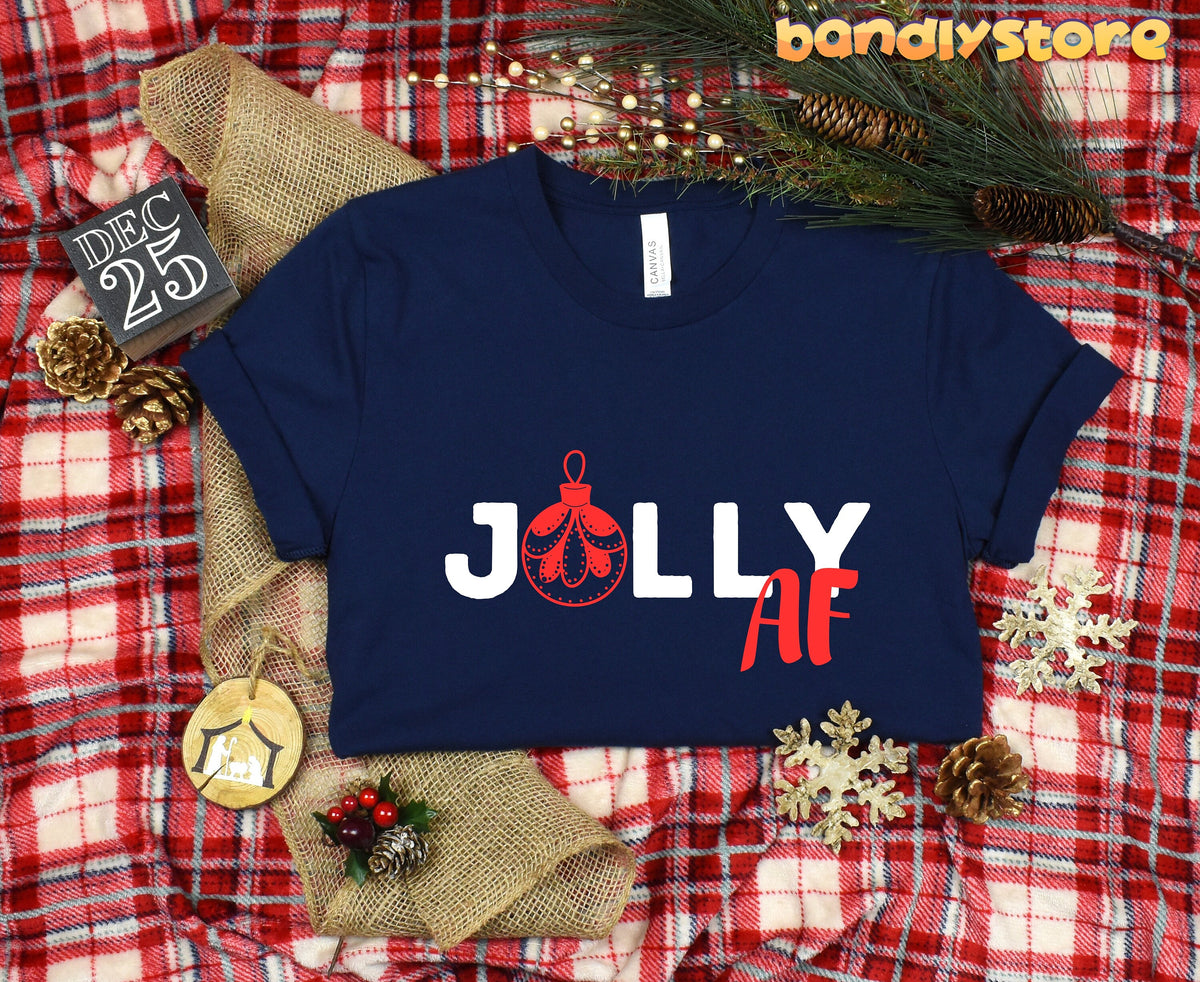 Jolly AF T-Shirt navy laid flat on plaid with pine branches, pinecones, snowflakes, burlap and Dec 25 sign.