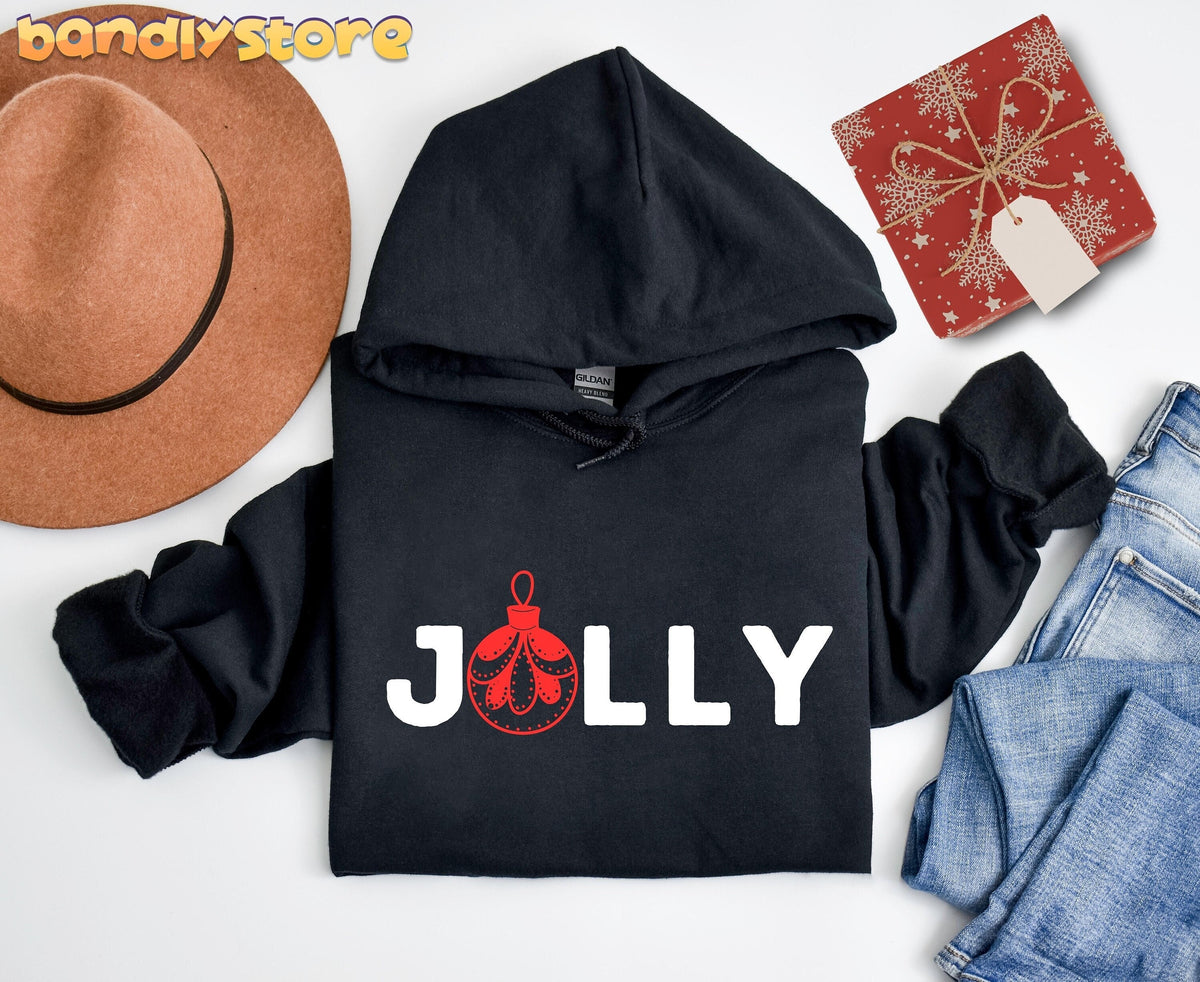 Feeling Jolly Christmas Hoodie in black, flat-lay with brown hat, red gift box and blue jeans.