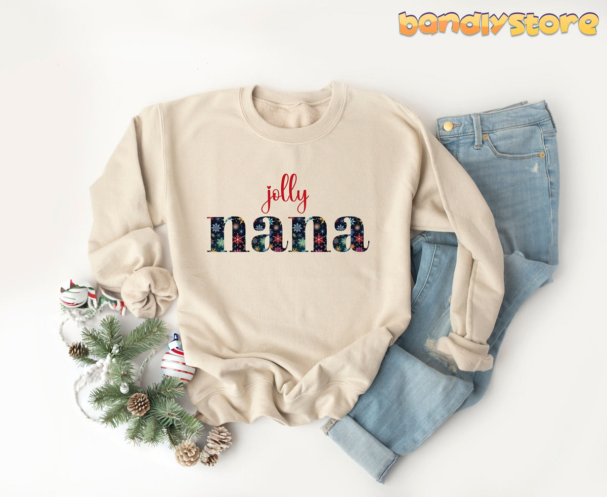 Jolly Nana Sweatshirt in sand laid flat on white with jeans, pine branches and ornaments.