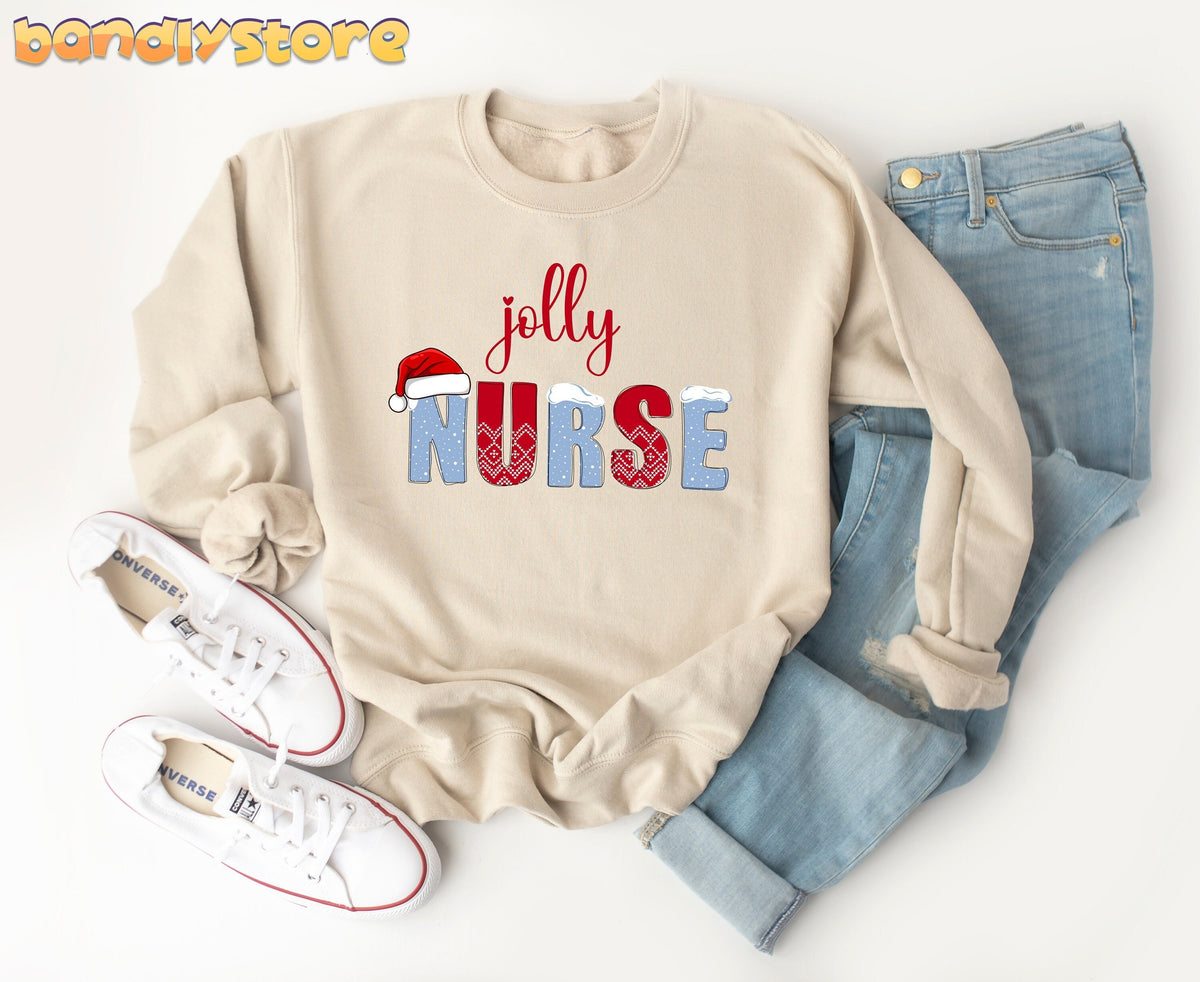 Jolly Nurse Sweatshirt in sand laid flat beside jeans and white sneakers on a white surface.