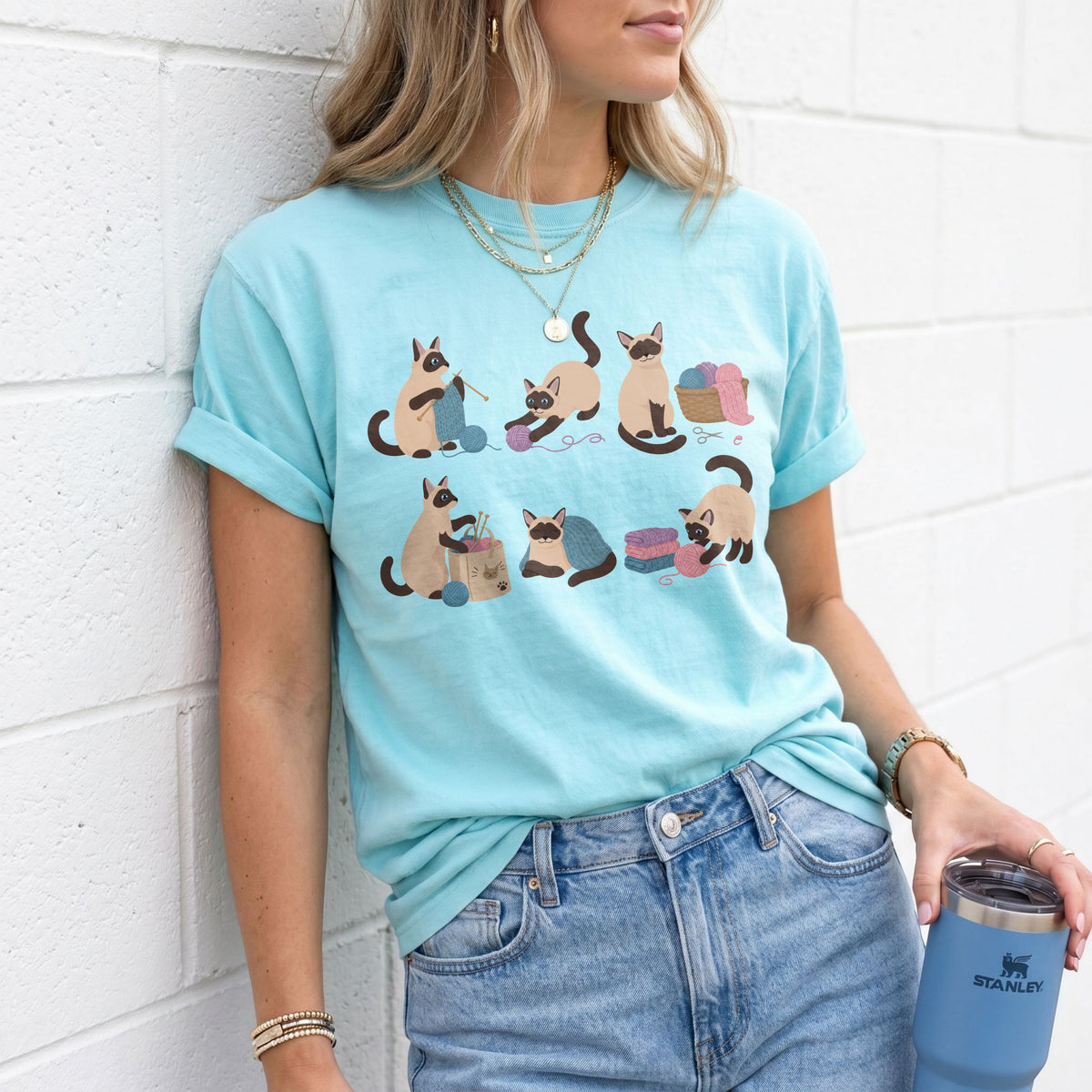 Funny Knitting Siamese Cats T-Shirt in Chalky Mint on a woman leaning against a white brick wall holding a tumbler.
