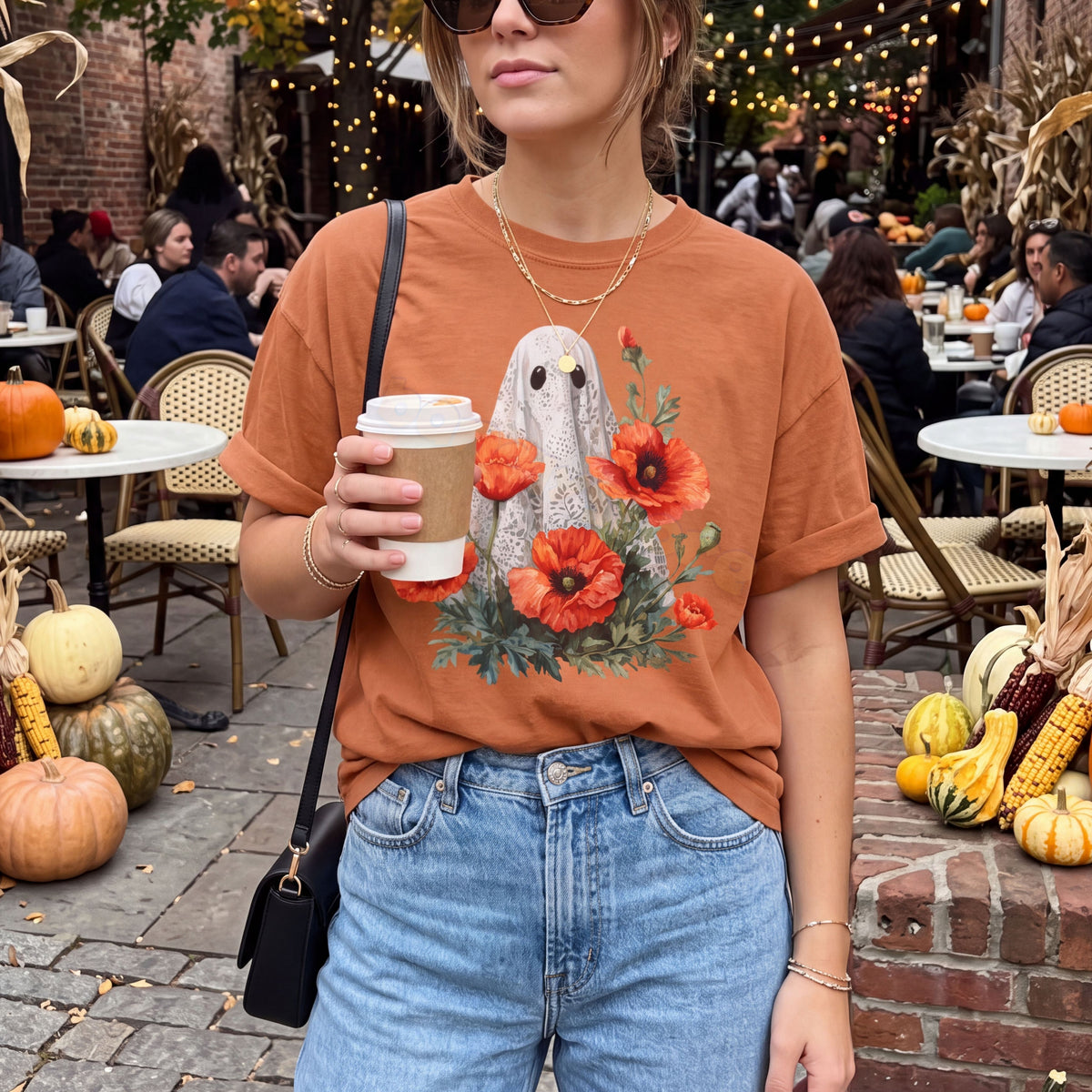 Vintage Lace Ghost Poppies T-Shirt in yam, front view at outdoor cafe patio surrounded by pumpkins and string lights.