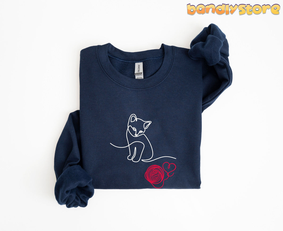 Line Art Kitten Sweatshirt in navy, folded flat on white with white cat line art and red yarn ball.