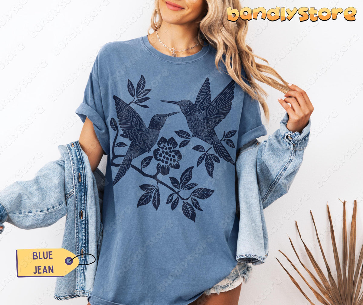 Linocut Hummingbird T-Shirt in Blue Jean, worn front-facing with denim jacket and dried palm frond nearby.