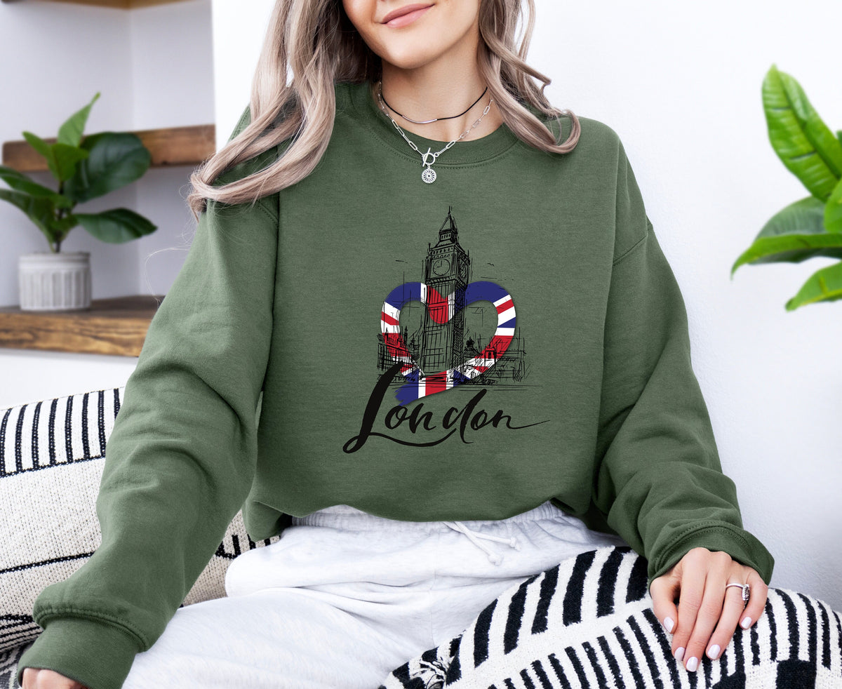 London Big Ben Sweatshirt in military green worn by a woman sitting on a couch beside plants and shelves.
