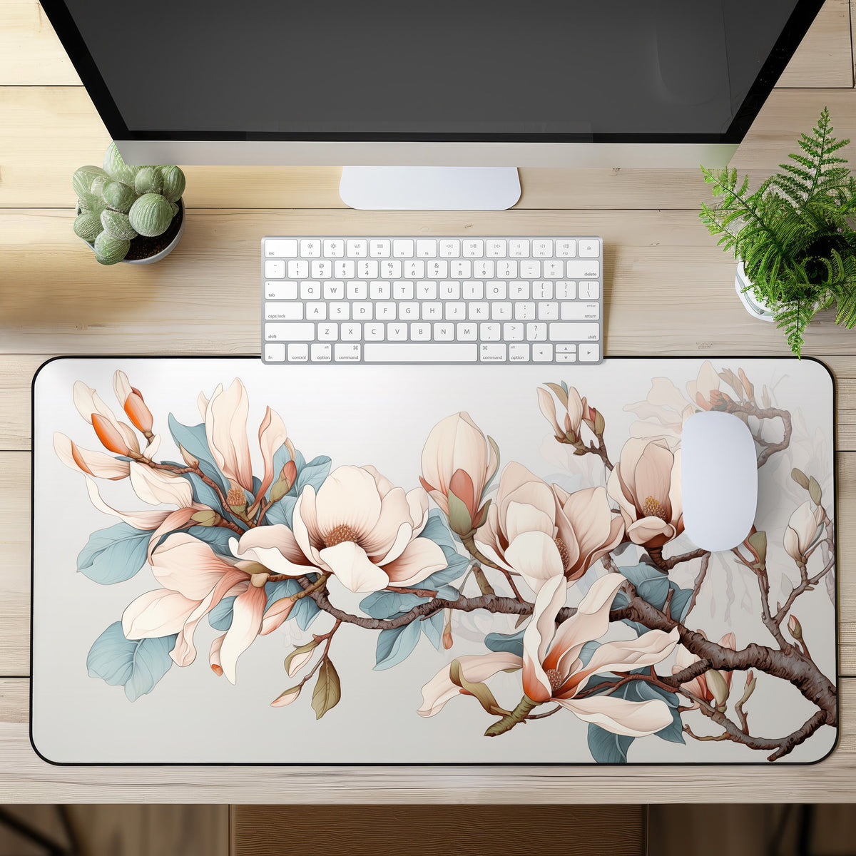 Magnolia Flowers Desk Mat in top-down view on a wooden desk with monitor, keyboard, mouse and plants.