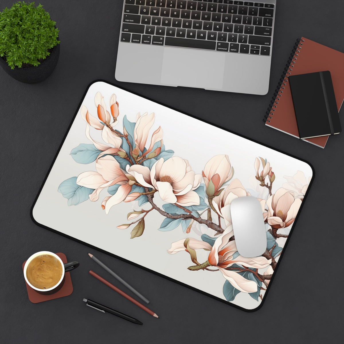 Magnolia Flowers Desk Mat 12 × 18 inches in top-down view on a desk with laptop, plant, coffee, notebooks and mouse.