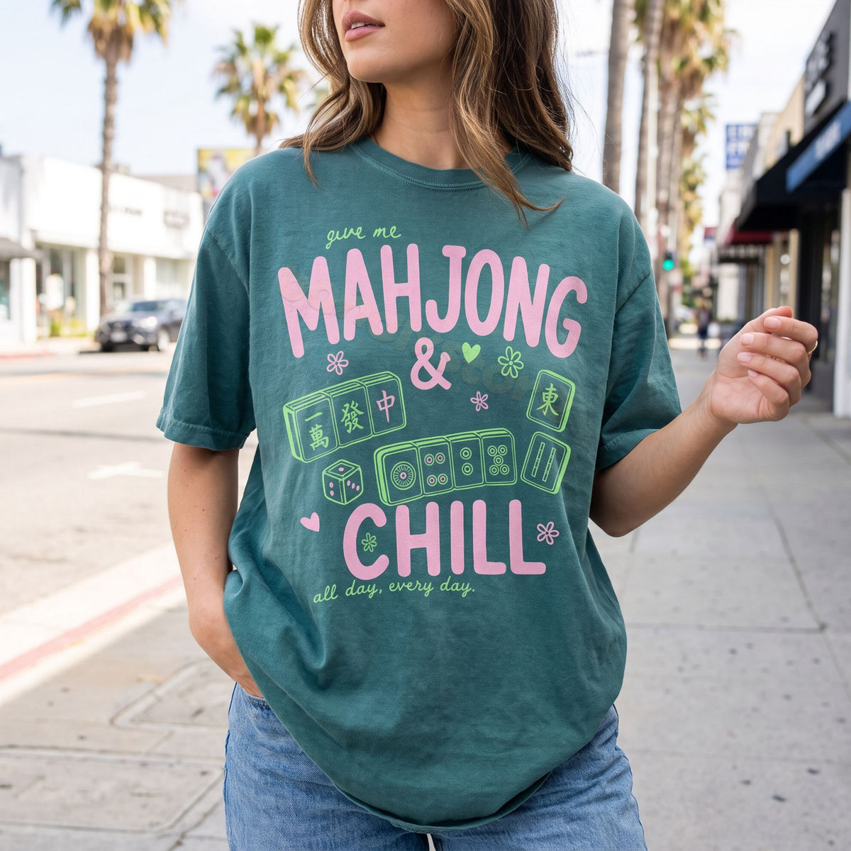 Mahjong And Chill T-Shirt in Blue Spruce on a model facing forward on a city sidewalk with palm trees and buildings.