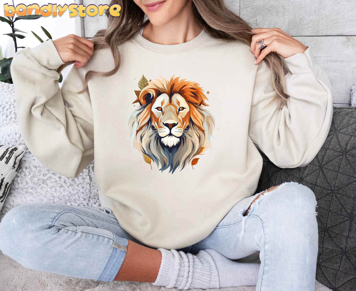 Majestic Lion Sweatshirt in sand, front view on a woman seated holding the shoulders beside plant and pillows.