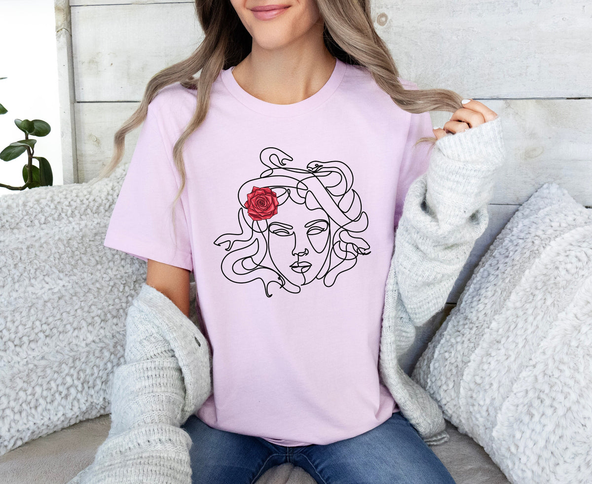 Medusa Head T-Shirt in pink on a person seated on white cushions against a wood wall with plant.